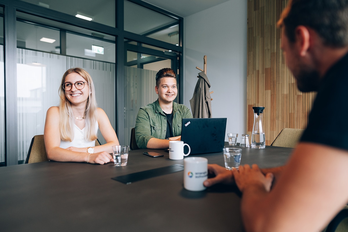 Eine junge Frau und ein junger Mann sitzen lachend in einem Büro.